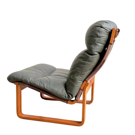 The Tessa Vintage Single No Arm Monaco Armchair – Forest Green (Revive) features green leather cushions with leather accents and a wooden frame, styled in mid-century fashion and photographed from the side against a plain gray background.