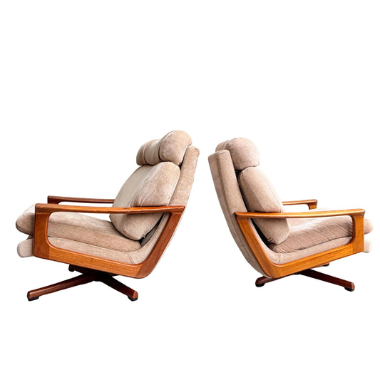 Two Vintage Mid Century Tessa T21 Swivel Chairs (Revive) with beige cushions and wooden frames are positioned back-to-back on a concrete floor against a light grey wall.