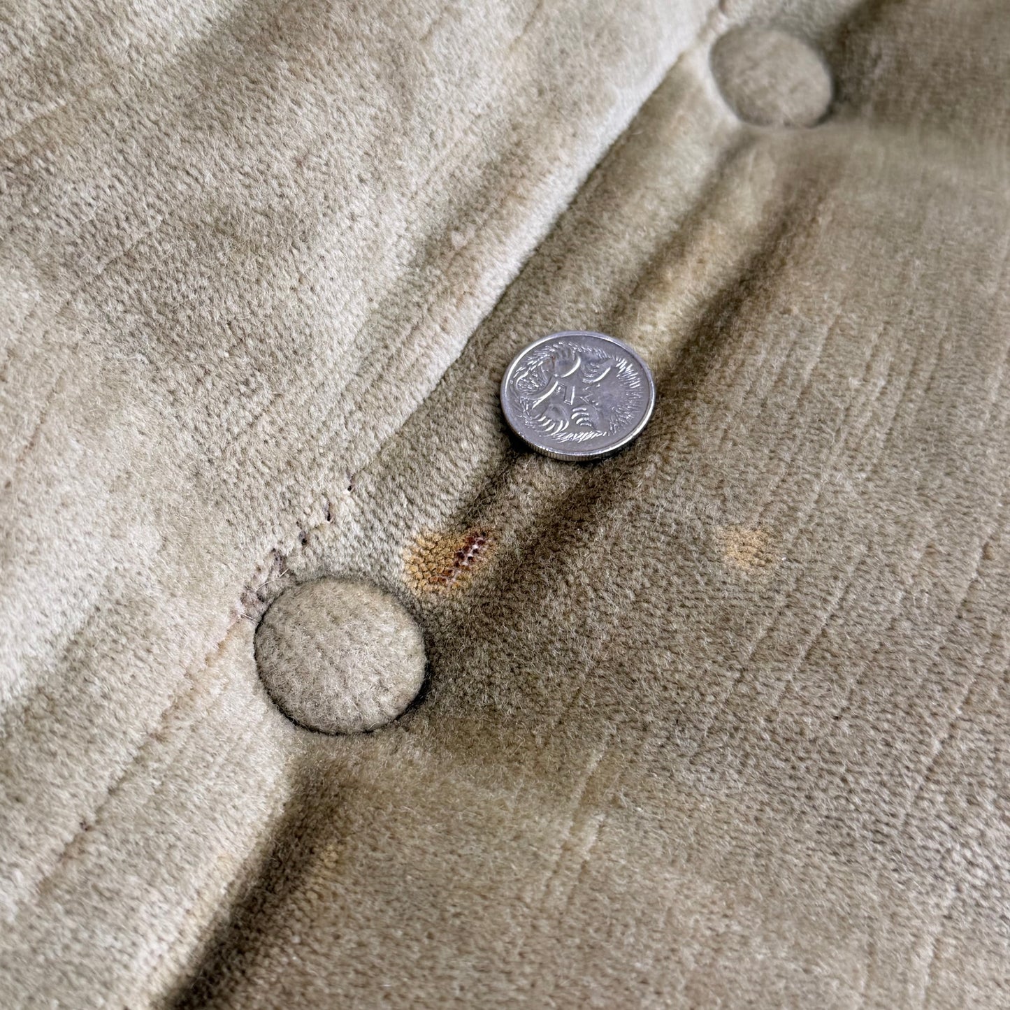 A U.S. quarter coin rests on the tufted olive green velvet of a Vintage Adrian Pearsall Style 1970s Rattan Designer Barrel Chair, with visible buttons and a faint stain near the coin.