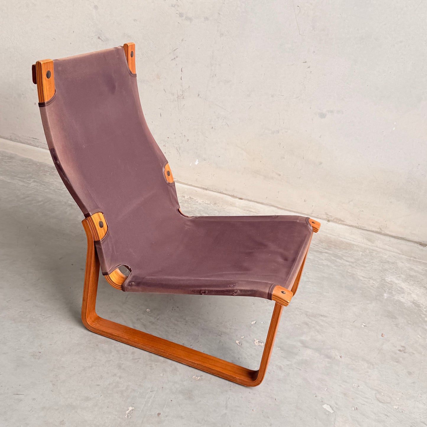 The Tessa Vintage Single No Arm Monaco Armchair – Forest Green (Revive) features a minimalist, angular wooden frame with forest green seat and subtle accents, its exposed joints standing out against a light concrete floor and wall.