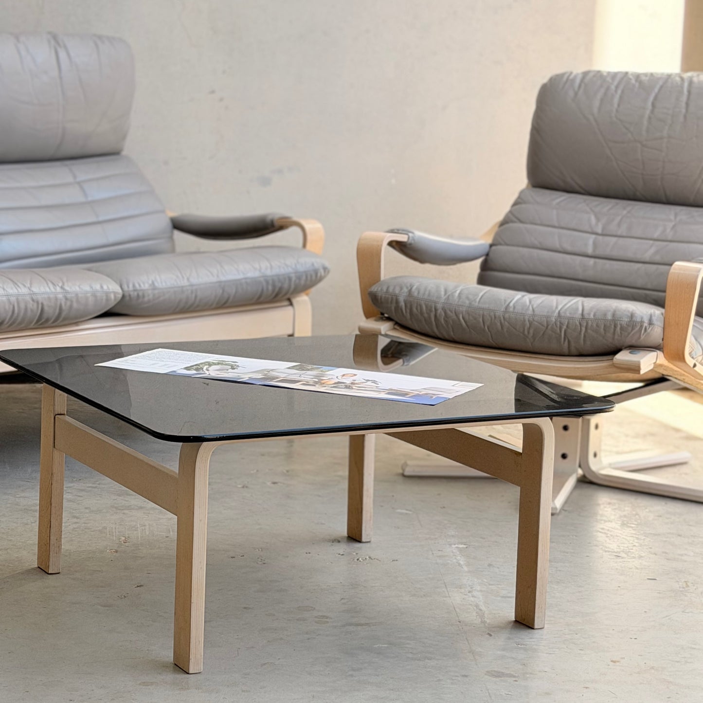 A modern lounge area showcases the Tessa Ferrara Lounge Suite – Complete 5-Piece Set (Revive), featuring mid-century charm with gray cushioned armchairs, a square glass coffee table, and light floors for an elevated Australian designer look.