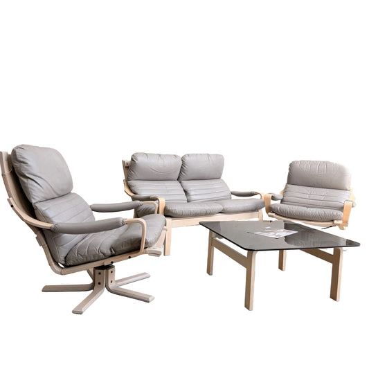 A minimalist room with light walls showcases the Tessa Ferrara Lounge Suite – Complete 5-Piece Set (Revive) in light wood and gray, paired with a glass coffee table holding papers. A wooden cabinet is partially visible in the background.