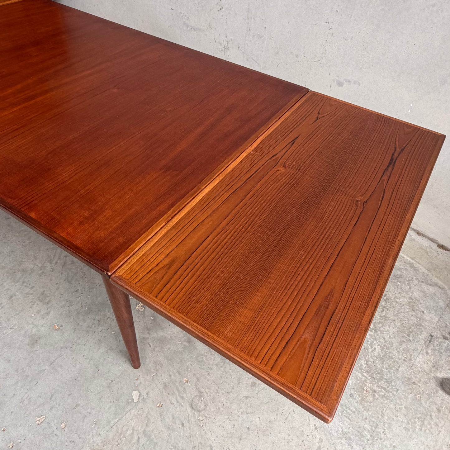 A close-up of the Vintage Mid-Century Parker 109 Nordic Extension Dining Table – Table Only (Revive), showcasing its warm reddish-brown wood grain and extended leaf, set against a plain concrete background.