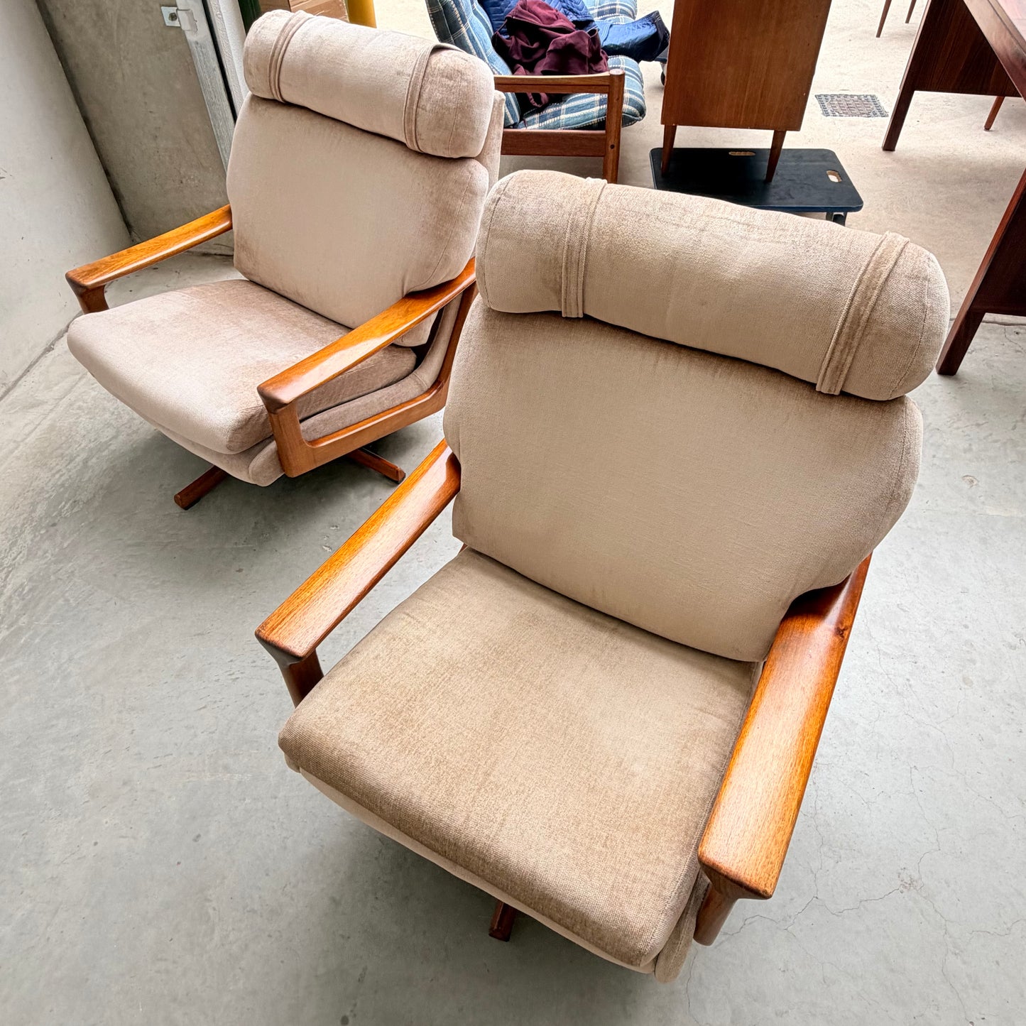 Two Vintage Mid Century Tessa T21 Swivel Chairs (Revive) in cream velvet with wooden arms and legs are angled on a concrete floor. Their padded backs and seats add comfort, highlighting classic mid-century style in this well-lit space.