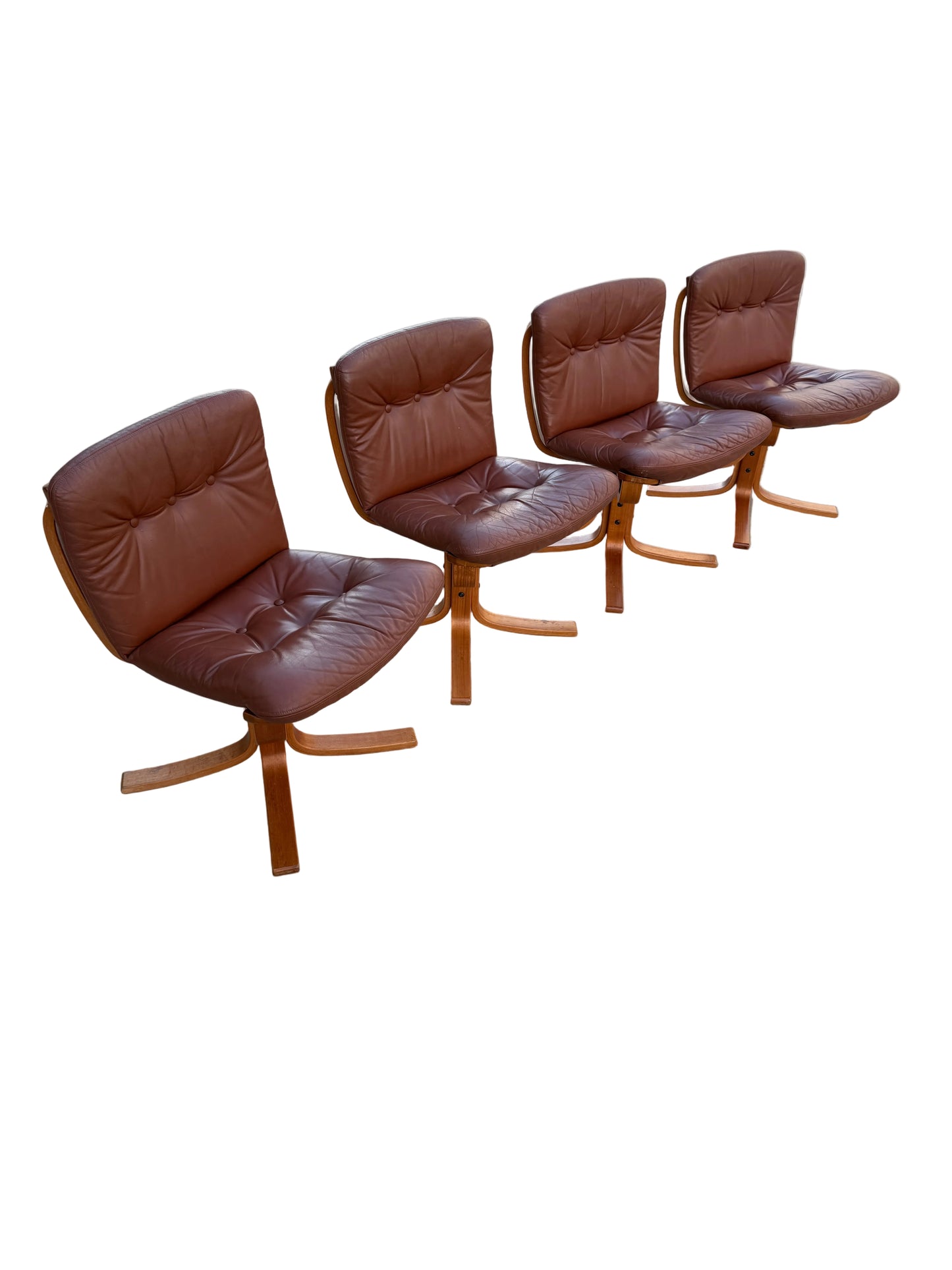 A Rare Set of 4 Vintage Joe Rufenacht Lounge Chairs in Howe Leather, featuring sleek wooden legs, are arranged on a concrete surface outdoors, with a white car and painted wall enhancing their Scandinavian-inspired appeal.