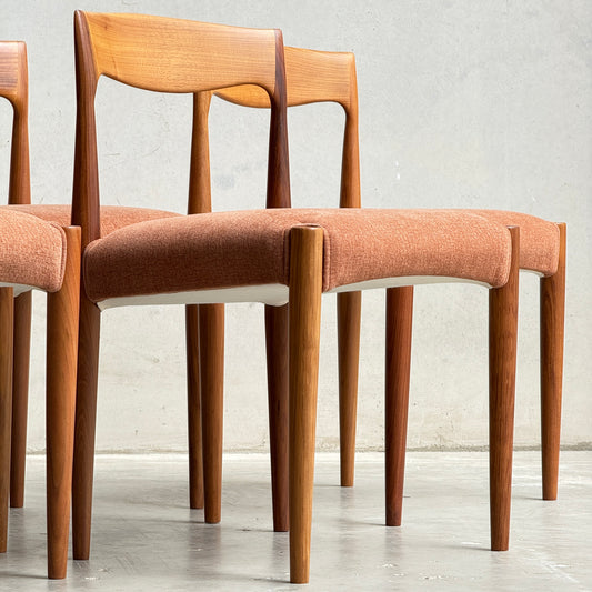 A set of four Fully Restored THB 'Milan' Dining Chairs (Rediscover) showcases curved backrests, tapered legs, and muted orange upholstery. These Australian mid-century chairs are displayed on a light grey floor against a plain light wall.