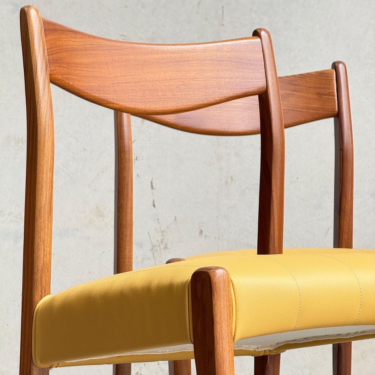 Two Fully Restored THB 'Stockholm' Dining Chairs from the set of 4 (Rediscover) with curved backrests and yellow cushions are side by side against a plain, light wall. They feature warm, polished Tasmanian blackwood.