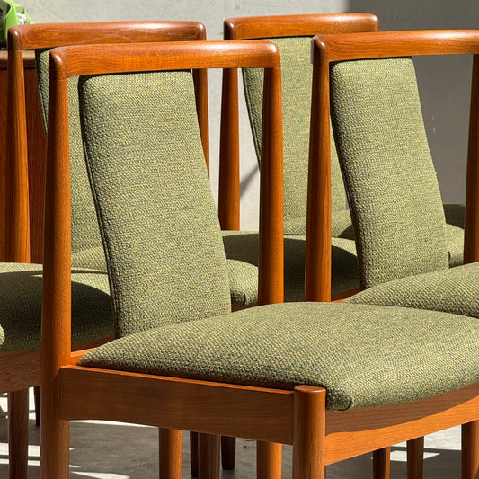Six fully restored Parker T-Back Number 88 dining chairs in forest green upholstery are arranged close together in natural sunlight, showcasing the iconic mid-century design of this Rediscover set.
