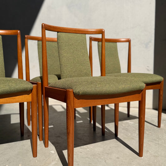 Four fully restored Parker T-Back Number 88 dining chairs in Forest Green (Rediscover) are arranged in sunlight against a light gray wall, their distinct shadows stretching across the floor.