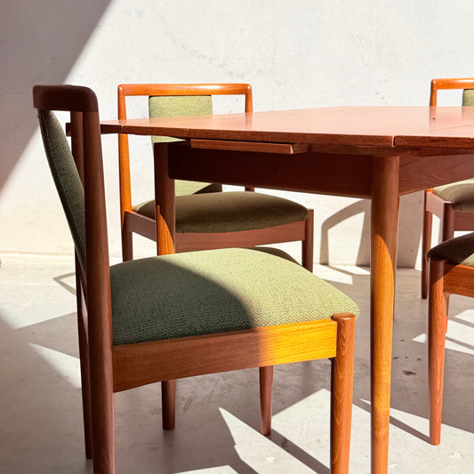 The Fully Restored Parker Dining Suite 5 Piece - Forest Green (Rediscover) features Scandinavian-inspired wooden chairs with green upholstery and a matching table, arranged to catch natural sunlight.