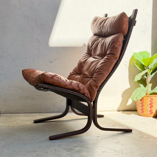 The Signature Vintage Ingmar Relling Siesta Set—two lounge chairs and a rare coffee table—features curved wooden frames and brown leather, highlighting classic Scandinavian mid-century design in a bright space with a concrete floor and greenery.