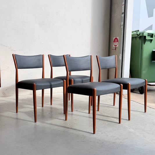 Four Parker Number 97 Dining Chairs Set of 4 – Licorice Vinyl are arranged in a row in a bright, minimalist space. A green trash bin and part of a white wall appear in the background.