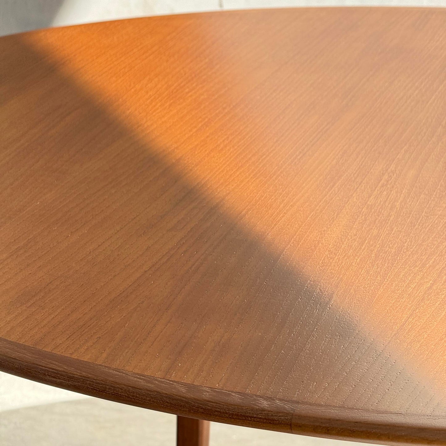 A Fully Restored Noblett Nordic Round MCM Table (Rediscover) sits partially in sunlight, casting a diagonal shadow over its smooth lacquered surface.
