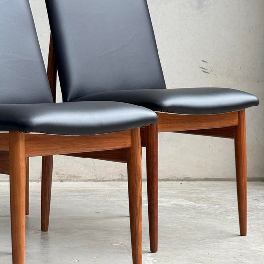 Two restored Parker 118 Slab Back Chairs with black leather seats and backs sit side by side on concrete, against a light gray wall. Shown here: Pre-Order Professional Restoration Parker 118 Chair Set of 4 (25% non-refundable deposit).