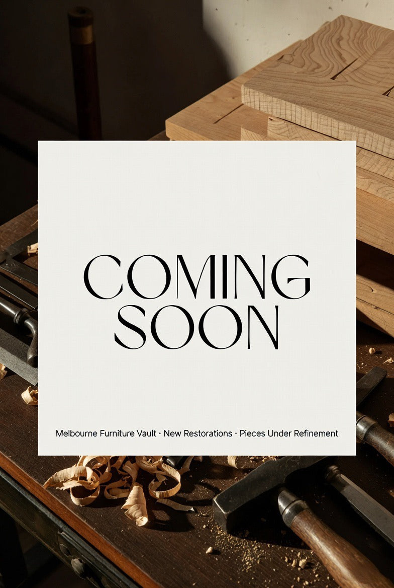 A sign reading COMING SOON sits on a woodworking table with wood shavings, tools, and wooden boards. Text below says Melbourne Furniture Vault · New Restorations · Pieces Under Refinement.