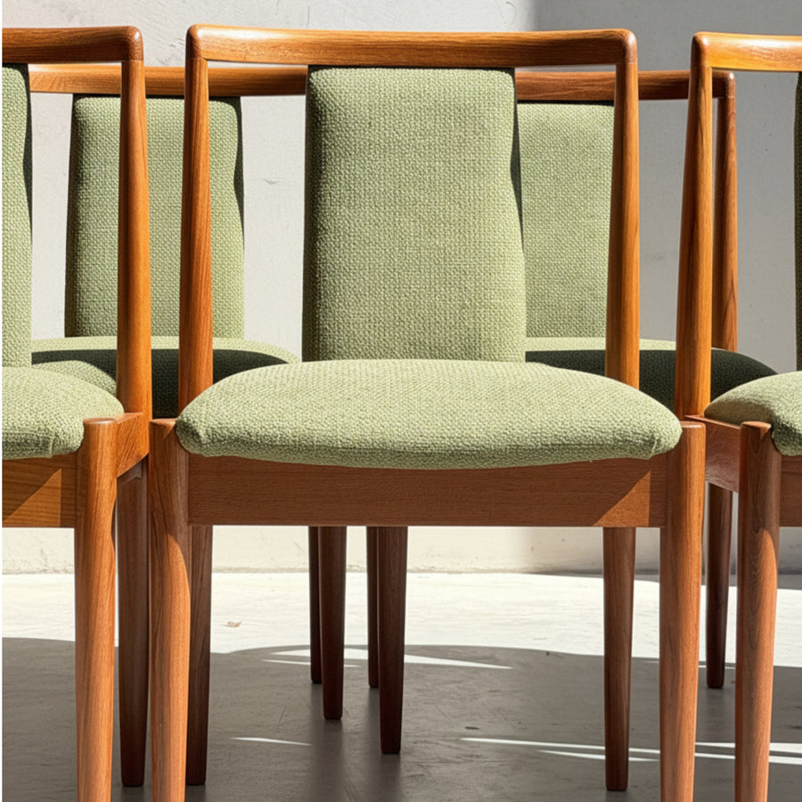 Four wooden dining chairs with light green upholstered seats and backrests are arranged closely together in bright natural light, casting distinct shadows on the floor.