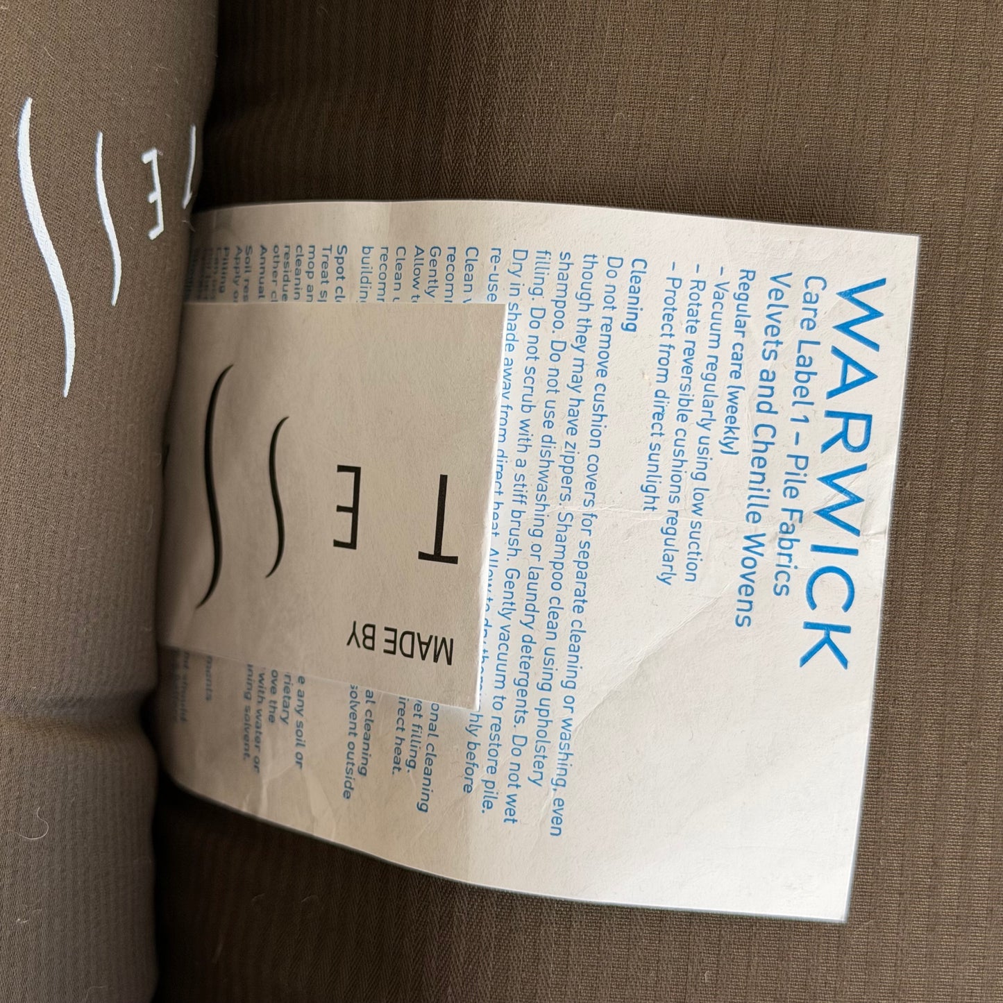 A fabric care label for a pair of Tessa Monaco Arm Chairs in sage green corduroy, with cleaning tips: vacuum regularly, keep fabric out of direct sunlight, and follow instructions for velvet and chenille woven fabrics.