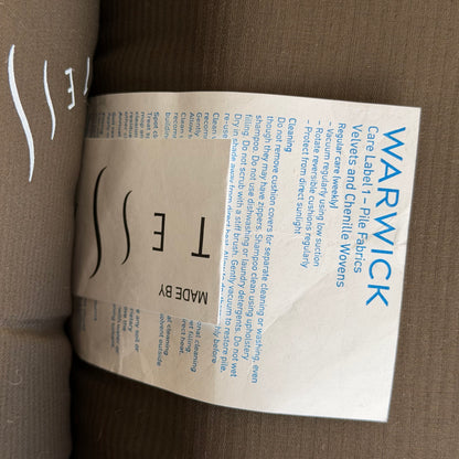 A fabric care label for a pair of Tessa Monaco Arm Chairs in sage green corduroy, with cleaning tips: vacuum regularly, keep fabric out of direct sunlight, and follow instructions for velvet and chenille woven fabrics.