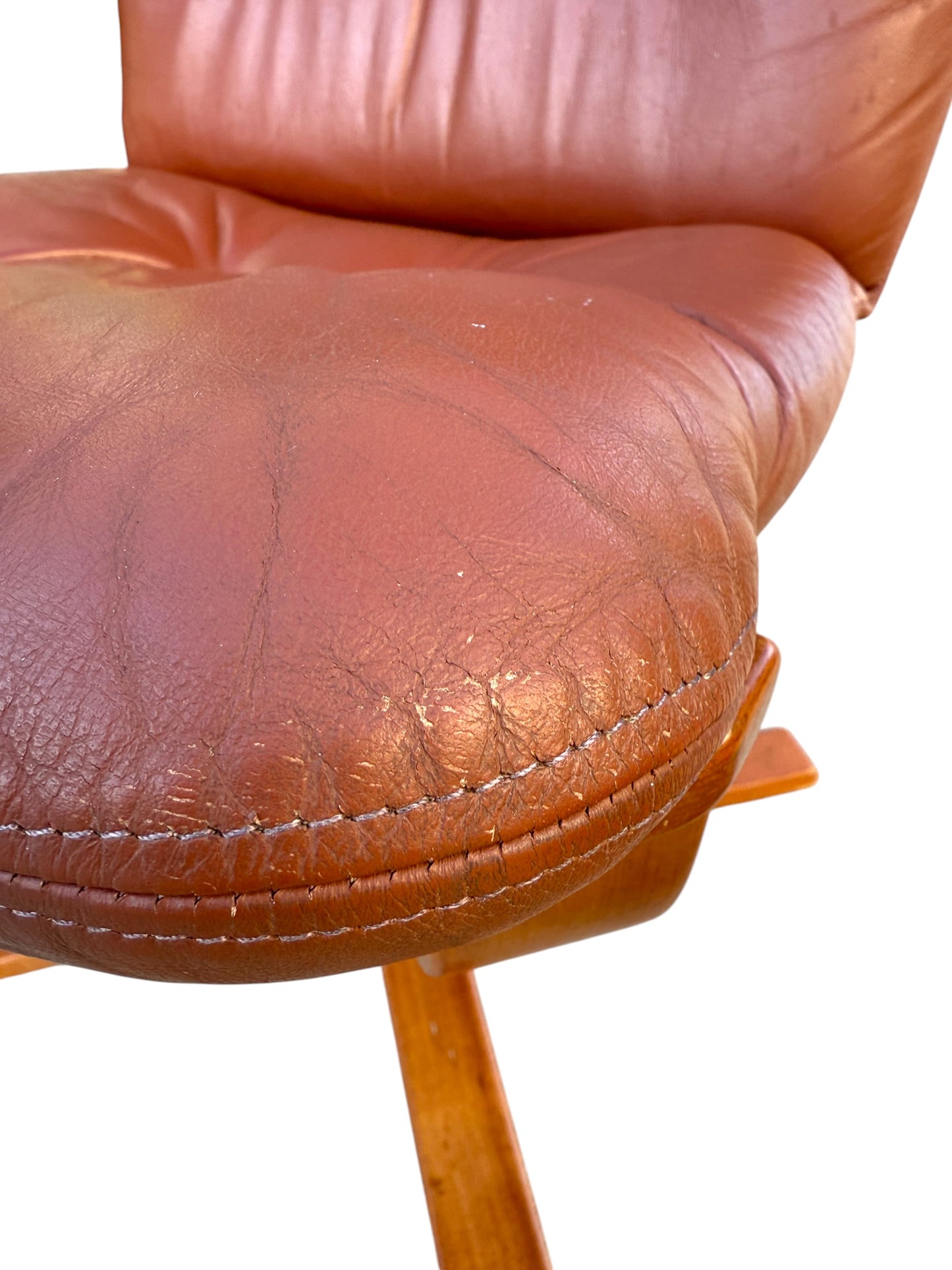 Close-up of a rare Howe Leather Joe Rufenacht lounge chair, showing brown leather seat with creases and stitching on wooden legs. From a set of 4 vintage Scandinavian design chairs, isolated on white background.