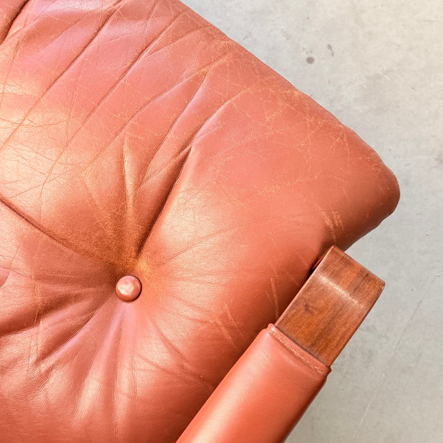 Close-up of a light brown leather cushioned seat with a button tuft and wrinkles, set in a wooden frame that reflects Fred Lowen’s mid-century style, seen in the Tessa T8 Lounge Suite modular two-seater sofa & armchairs (Revive).