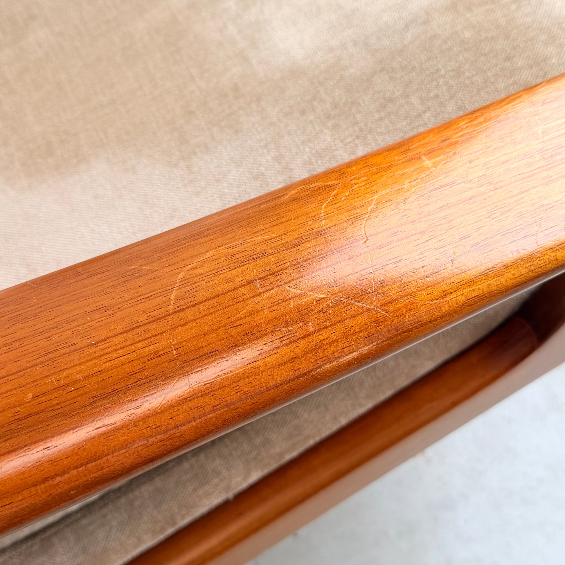 Close-up of a wooden armrest with light scratches and scuffs, attached to cream velvet upholstery. The polished, warm-toned wood reflects the style of the Vintage Mid Century Tessa T21 Swivel Chair (Revive).
