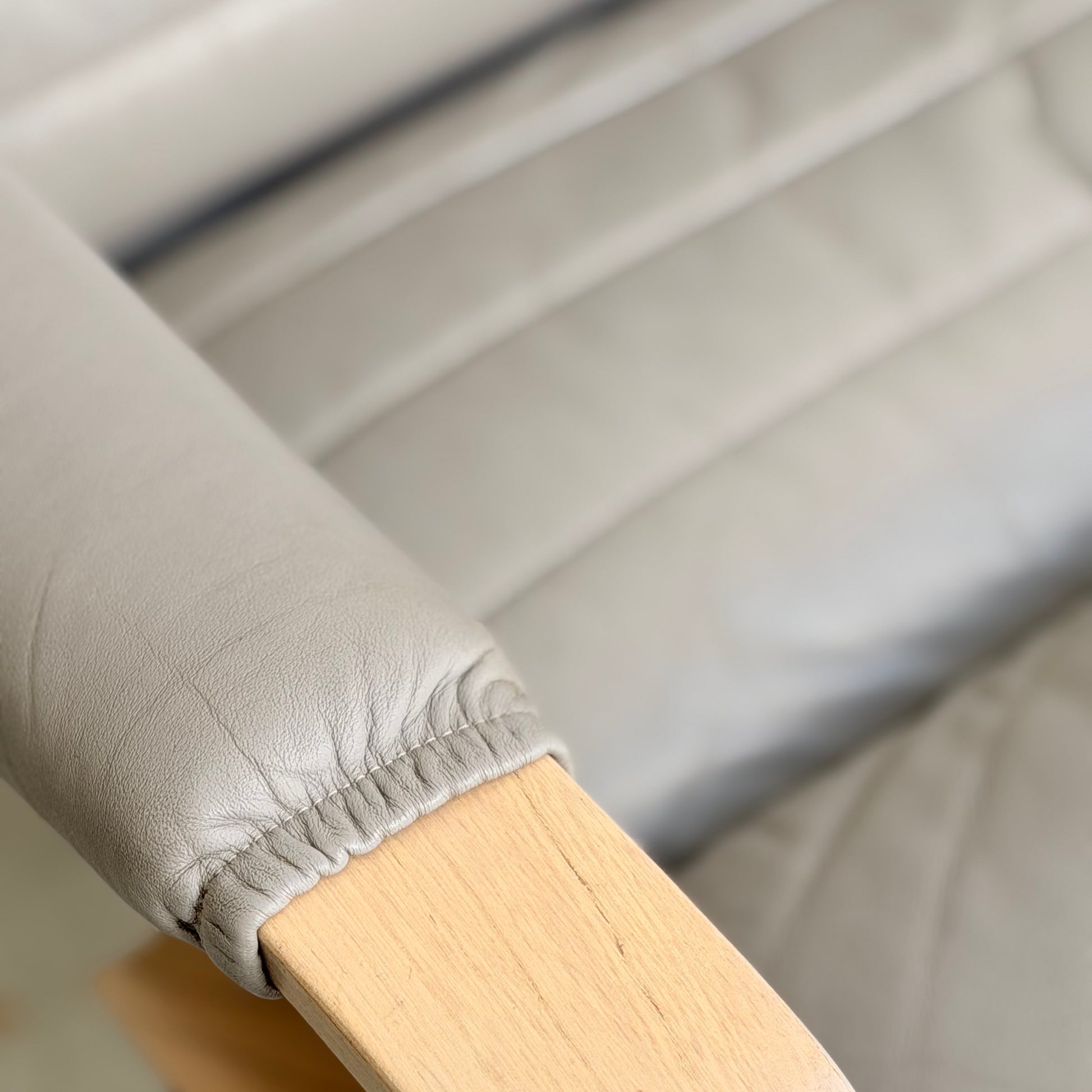 Close-up of a light gray cushioned chair with wooden armrest and visible stitching, showcasing the textured upholstery and mid-century modern style of the Tessa Ferrara Lounge Suite – Complete 5-Piece Set (Revive).