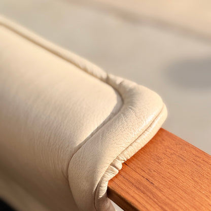 Close-up of a beige cushion wrapped around the wooden armrest of the Tessa Austin Blonde Leather Armchair (Revive), with soft natural light highlighting the texture of the materials.