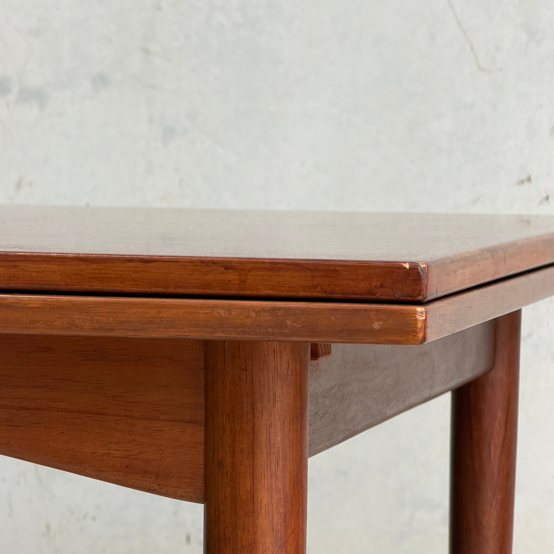 Close-up of the corner of a Vintage Mid-Century Parker 109 Nordic Extension Dining Table (Table Only, Revive), featuring rounded legs and a smooth, polished surface against a light, textured wall.