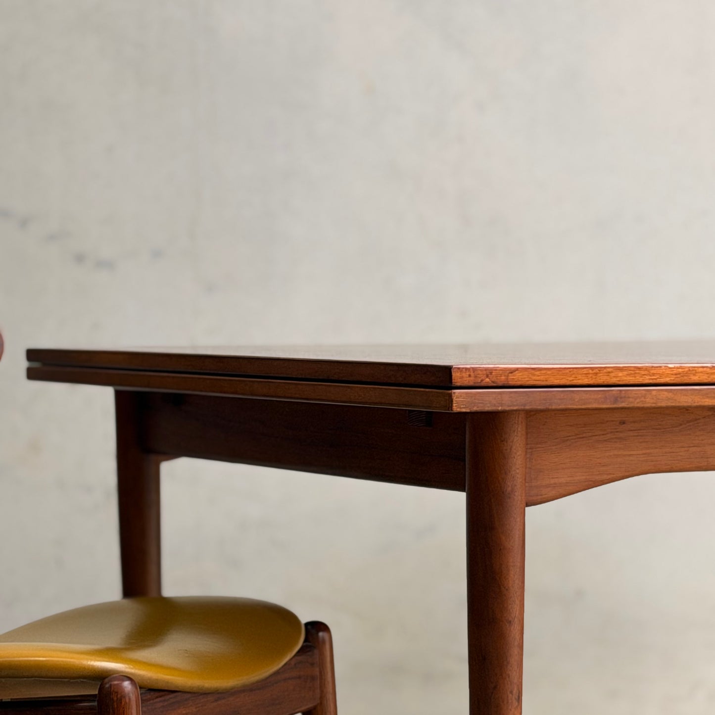 A close-up of the Vintage Mid-Century Parker 109 Nordic Extension Dining Table (Revive) featuring rounded edges, set against a plain, light-colored wall.