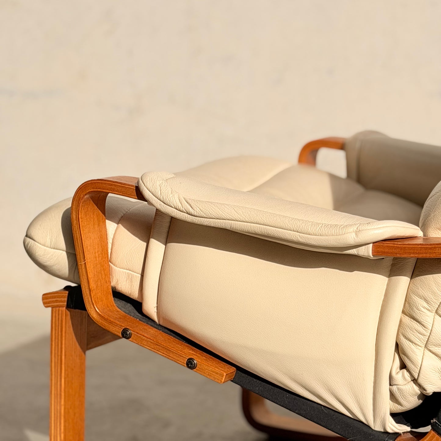 A close-up of the Tessa Austin Blonde Leather Armchair (Revive), featuring beige leather and wooden armrests, basking in warm sunlight against a neutral background.