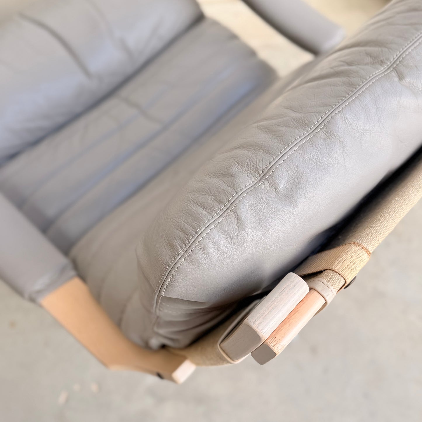 Close-up of a Pair of Tessa Ferrara Swivel Armchairs (Revive) in light gray with visible leather creases, wood armrest details, and beige fabric straps—showcasing classic vintage Tessa Furniture and mid-century Australian style.