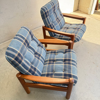 Two restored Domino Møbler armchairs with blue plaid cushions sit side by side on a concrete floor near a white wall and doorway in a brightly lit room.