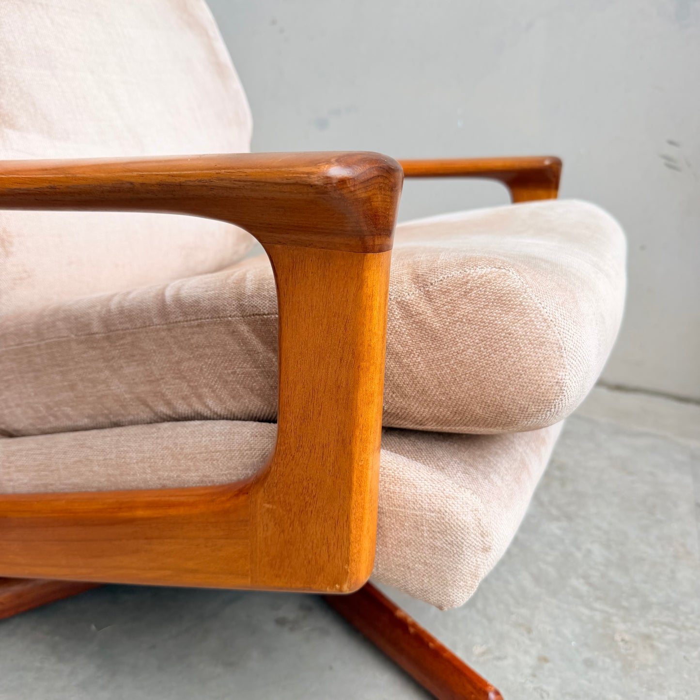 Close-up of the Vintage Mid Century Tessa T21 Swivel Chair (Revive), a cushioned beige armchair with polished wooden armrests and base, set on a concrete floor against a plain light gray wall.