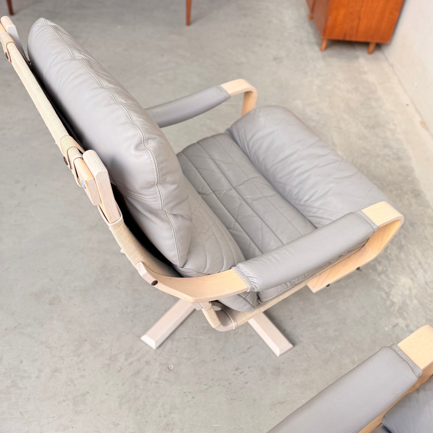 A pair of Tessa Ferrara Swivel Armchairs (Revive) with light wood frames and light gray leather quilted cushions sit on four-legged swivel bases, showcasing mid-century Australian design on a concrete floor.