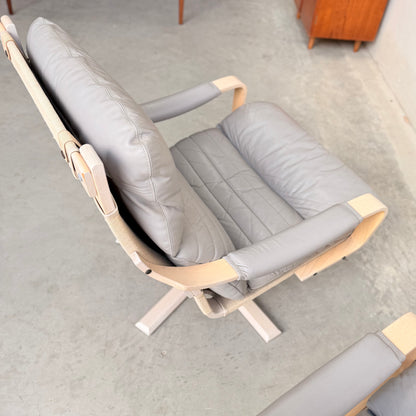 A pair of Tessa Ferrara Swivel Armchairs (Revive) with light wood frames and light gray leather quilted cushions sit on four-legged swivel bases, showcasing mid-century Australian design on a concrete floor.