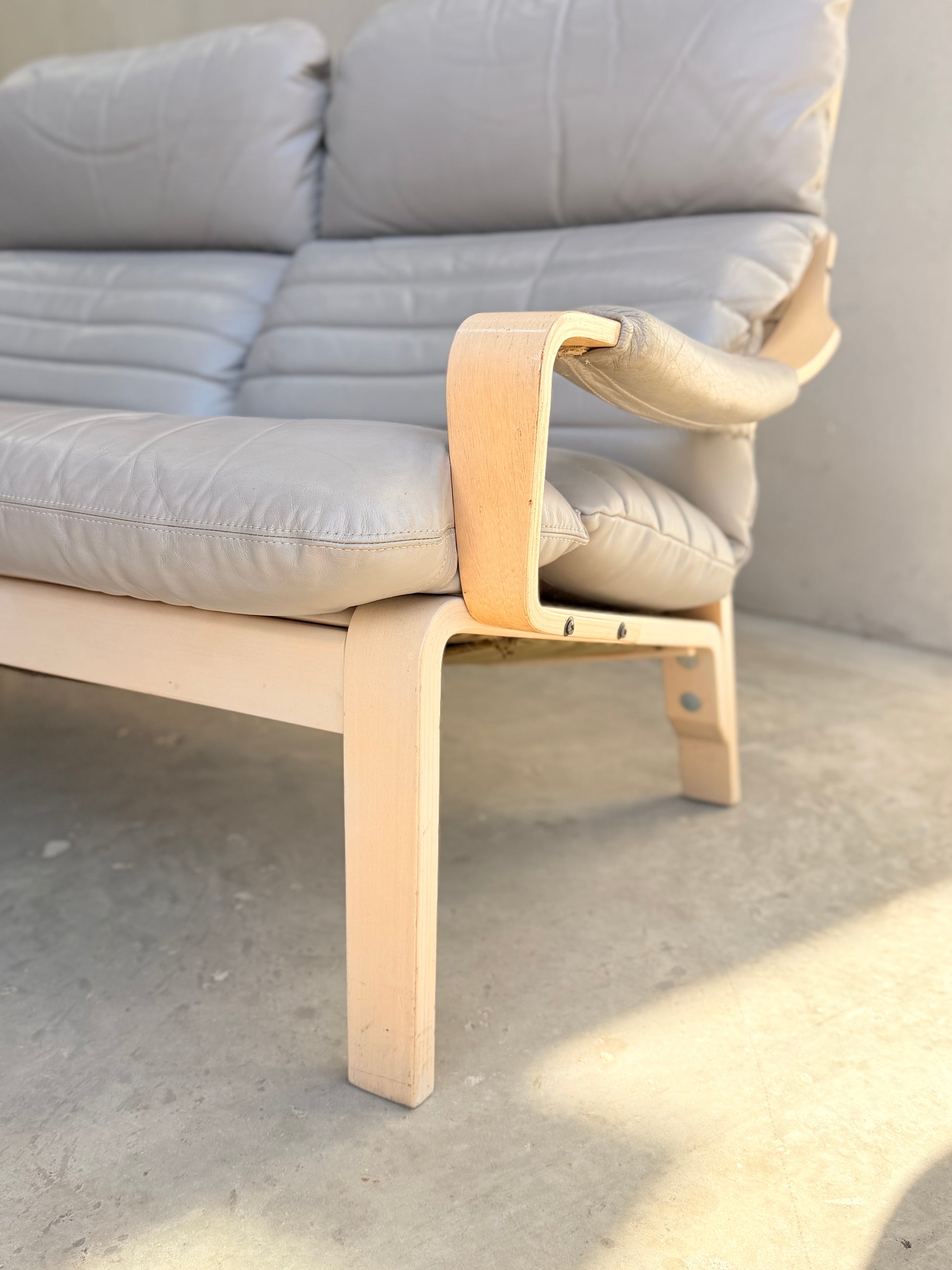 Close-up of the Tessa Ferrara Lounge Suite – Complete 5-Piece Set (Revive) with light wood frame, light grey tufted cushions, and curved armrests, inspired by mid-century modern design and shown in natural light on a smooth concrete floor.