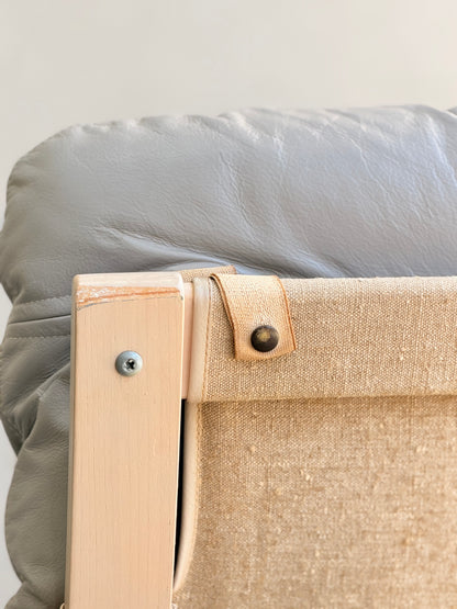 Close-up of the corner of a light wooden chair from the Tessa Ferrara Lounge Suite – Complete 5-Piece Set (Revive), featuring beige fabric, a buttoned strap, and gray cushion with mid-century modern details inspired by Fred Lowen.