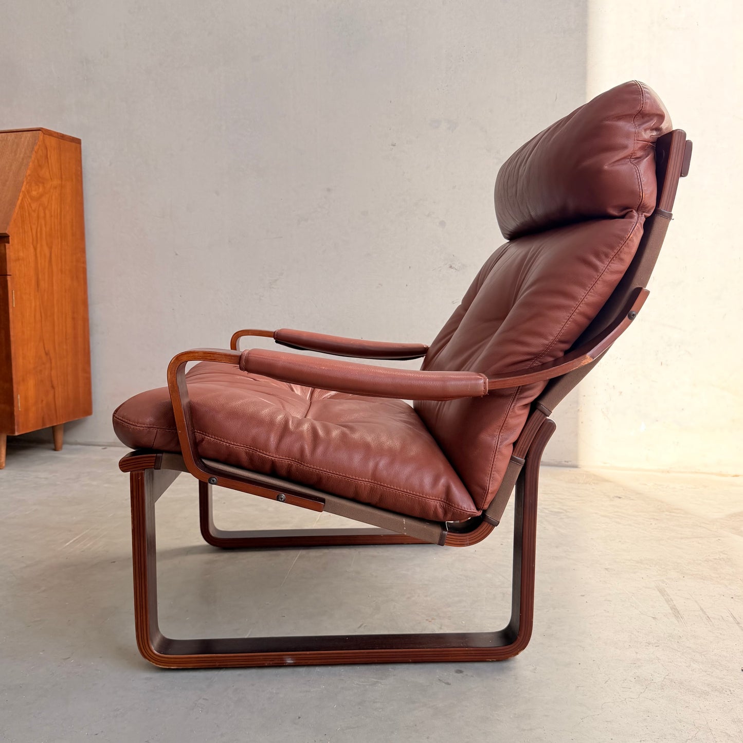 The Tessa T8 Lounge Suite modular two-seater sofa and armchairs (Revive) feature padded seats, armrests, and backrests on a wooden frame in mid-century style, set against a light wall with a wooden cabinet and natural light from the right.