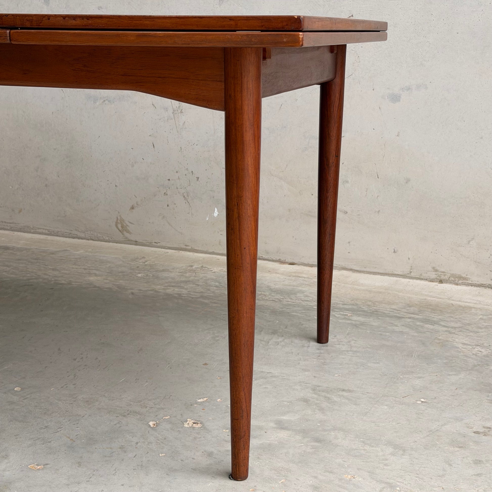 Close-up of the Vintage Mid-Century Parker 109 Nordic Extension Dining Table – Table Only (Revive) with tapered legs and a warm brown finish, set against a light concrete wall and floor for a classic look.