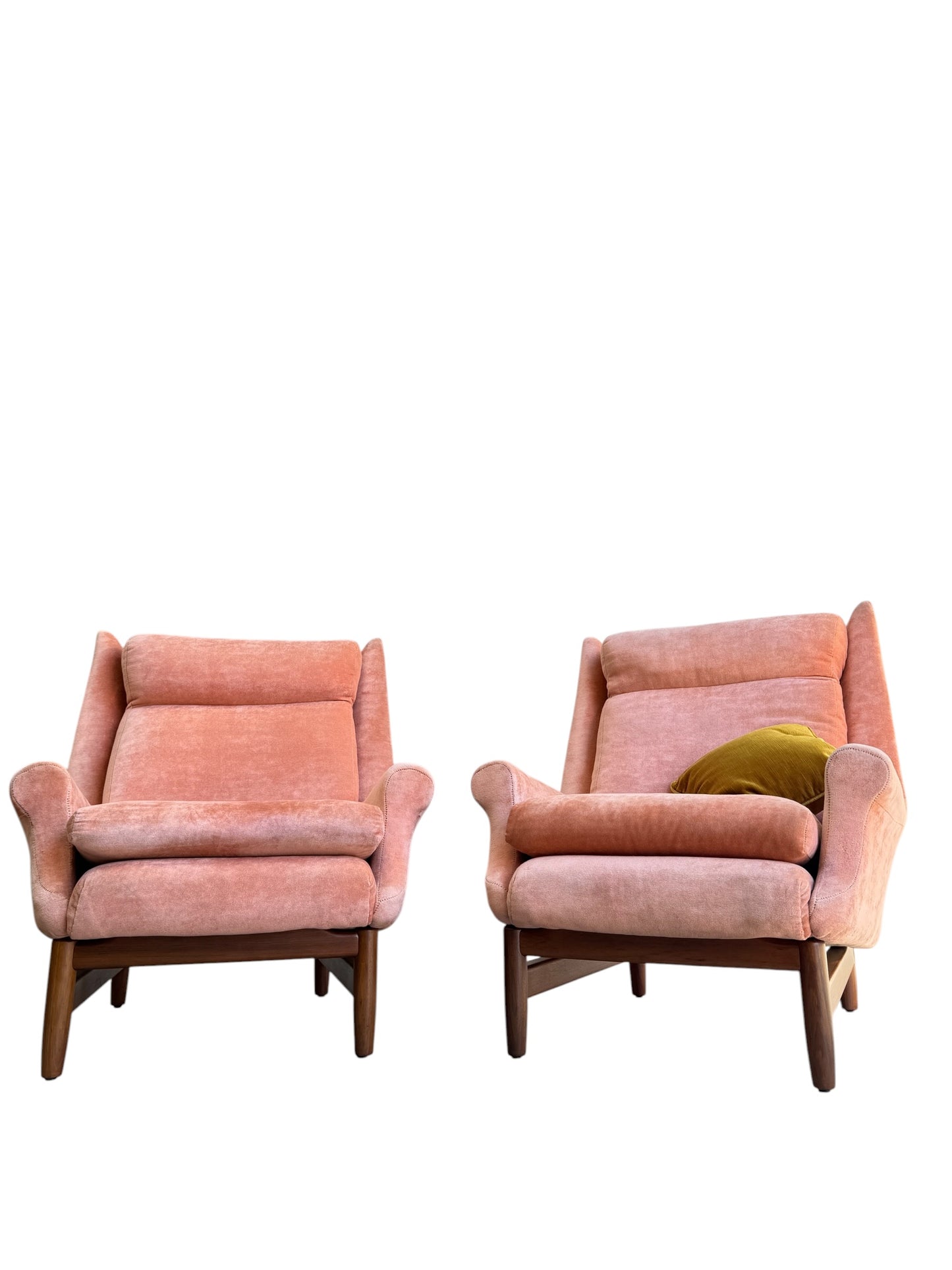 Two Mid-Century High-Back Armchairs in dusty pink velvet with Blackwood frames sit side by side, one featuring a green pillow, set against a white background.