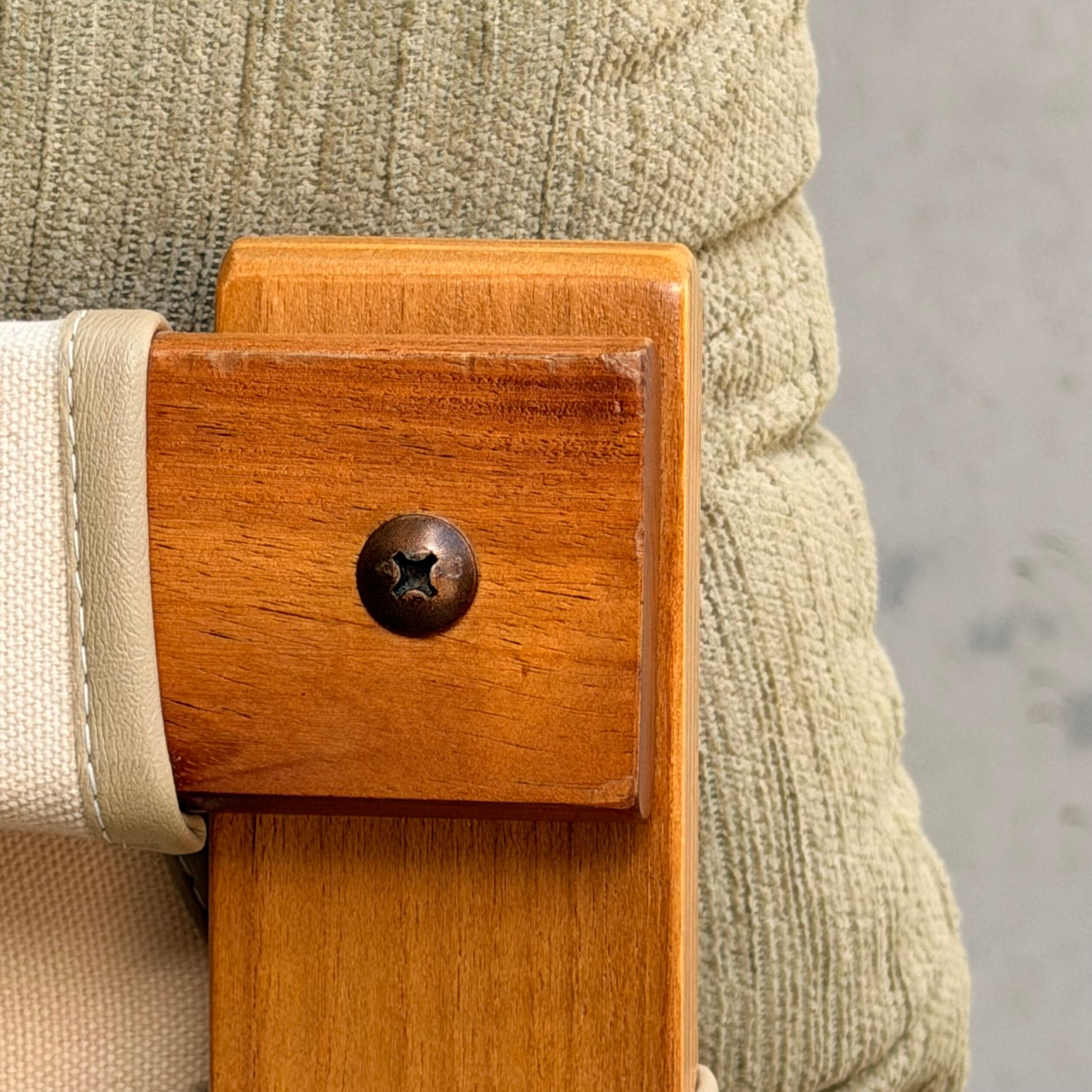 Close-up of a wooden chair with a metal screw, beige cushion, and light fabric strap set against gray—ideal to pair with the Pair of Tessa Monaco Arm Chairs - Sage Green Corduroy Like New (Revive).