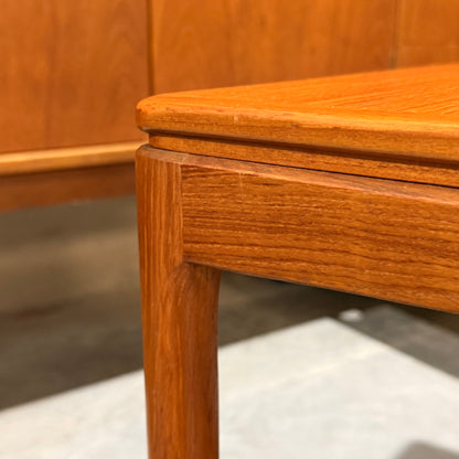 Close-up of a wooden table corner with smooth, rounded edges and visible grain, reflecting mid-century craft. In the blurred background is a Rare set of Alpa Teak Nesting Tables – Set of 3 - Australian Mid-Century Modern (Revive).
