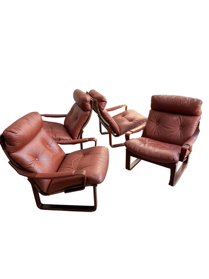 Three Tessa T8 Lounge Suite modular two-seater sofas and Revive armchairs, in vintage brown leather with padded seats and backs, are arranged on a light concrete floor against a plain wall in a well-lit indoor space.