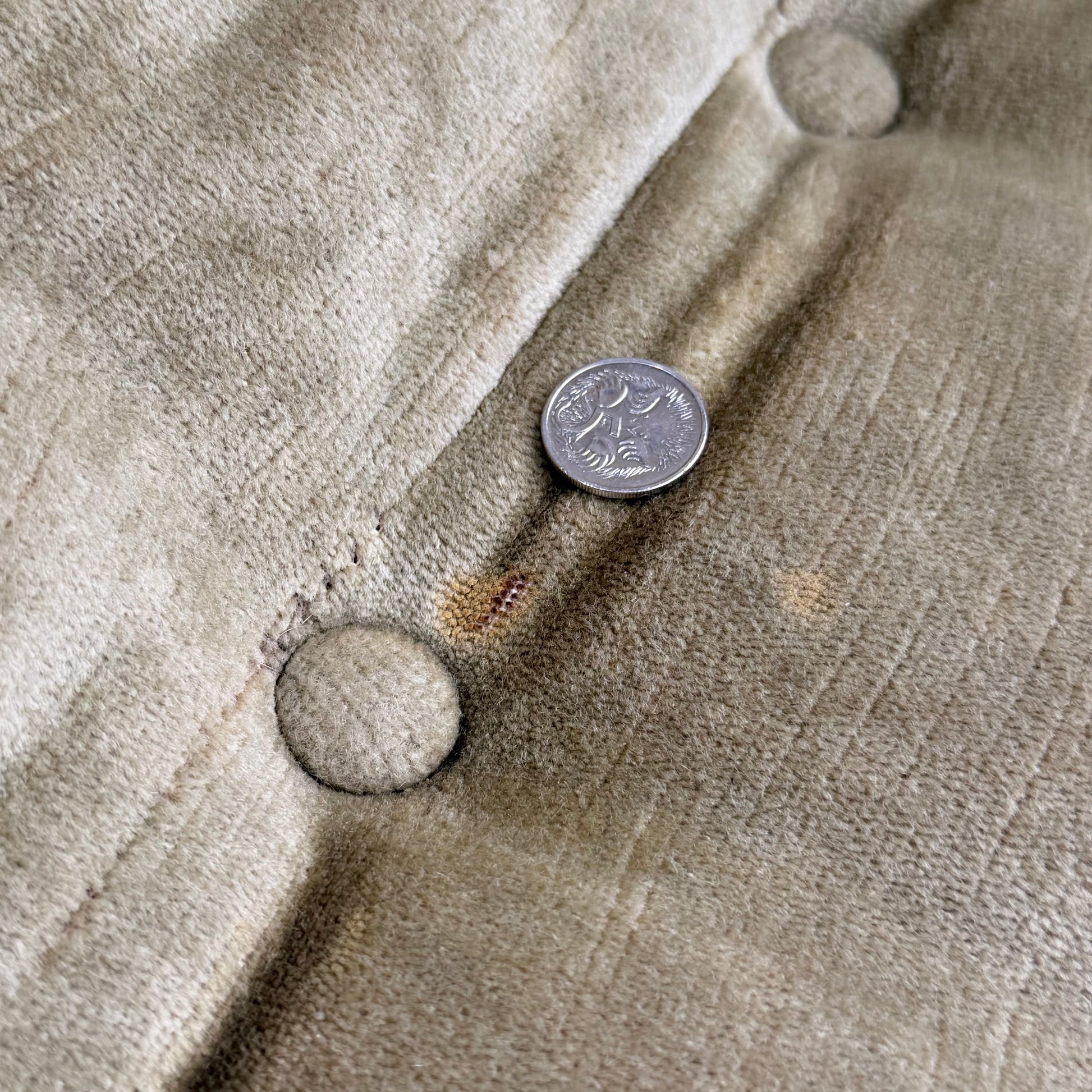 A U.S. quarter coin rests on the tufted olive green velvet of a Vintage Adrian Pearsall Style 1970s Rattan Designer Barrel Chair, with visible buttons and a faint stain near the coin.