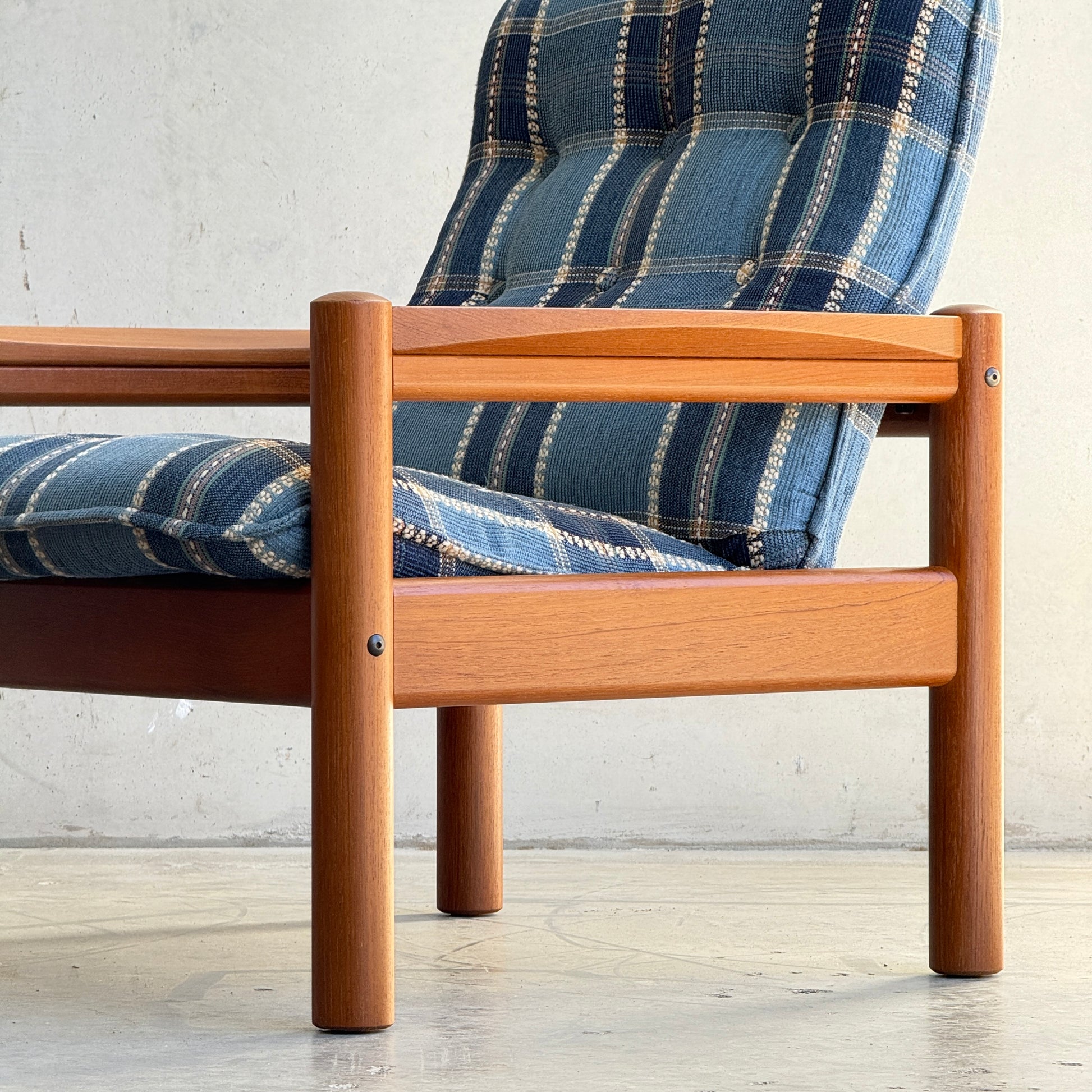 Close-up of a Restored Domino Møbler Armchair from the Blue Plaid Mid-Century Set (Rediscover), featuring a solid wood frame and retro plaid cushions, set against a light wall and concrete floor in classic Scandinavian style.