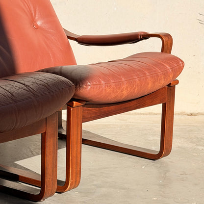 Two Tessa T8 Lounge Suite (Revive) modular armchairs, with reddish-brown leather cushions and wooden frames, sit side by side on a sunlit concrete floor.
