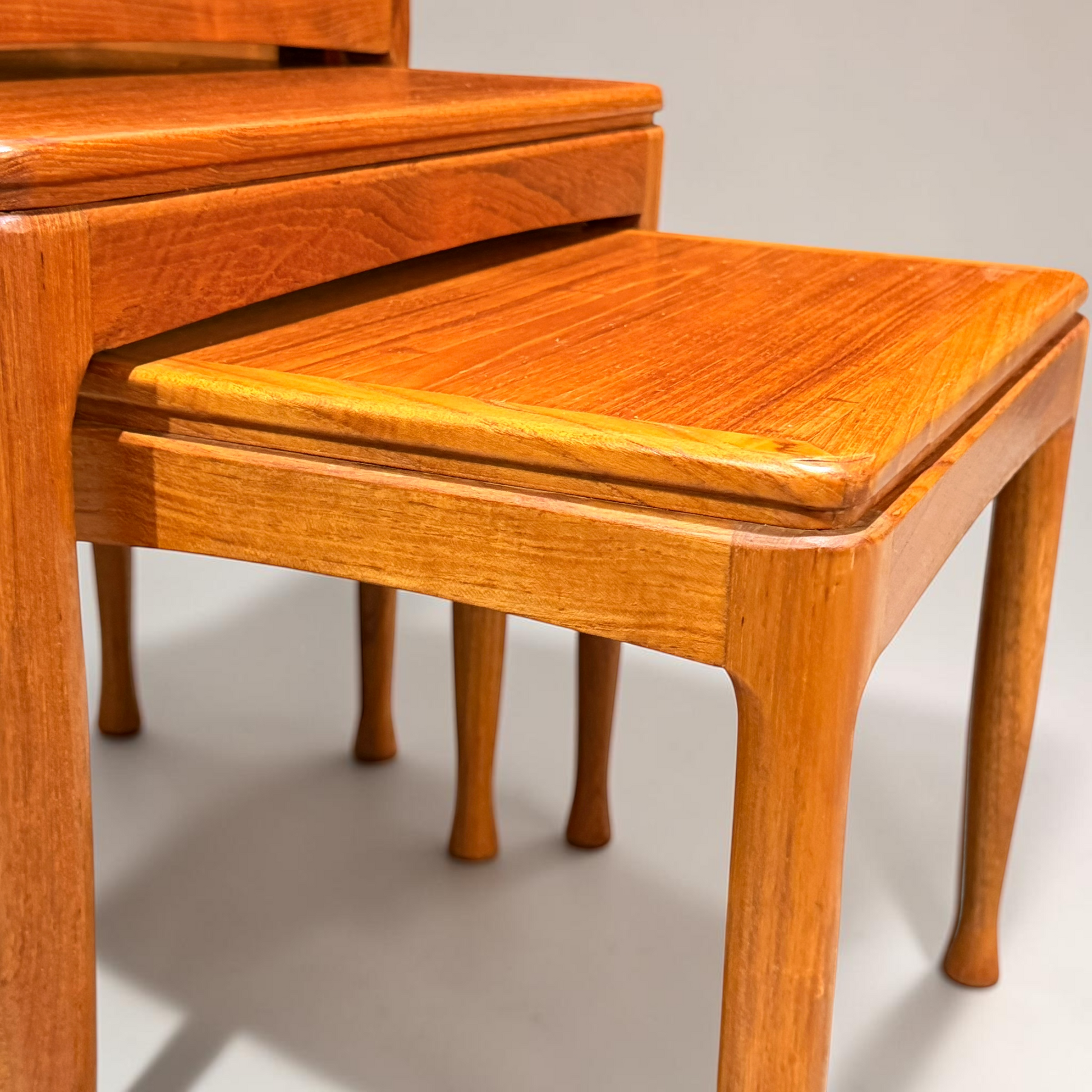 A close-up of the Rare set of Alpa Teak Nesting Tables – Set of 3 - Australian Mid-Century Modern (Revive), featuring polished teak surfaces, smooth edges, and curved legs, set against a plain background.