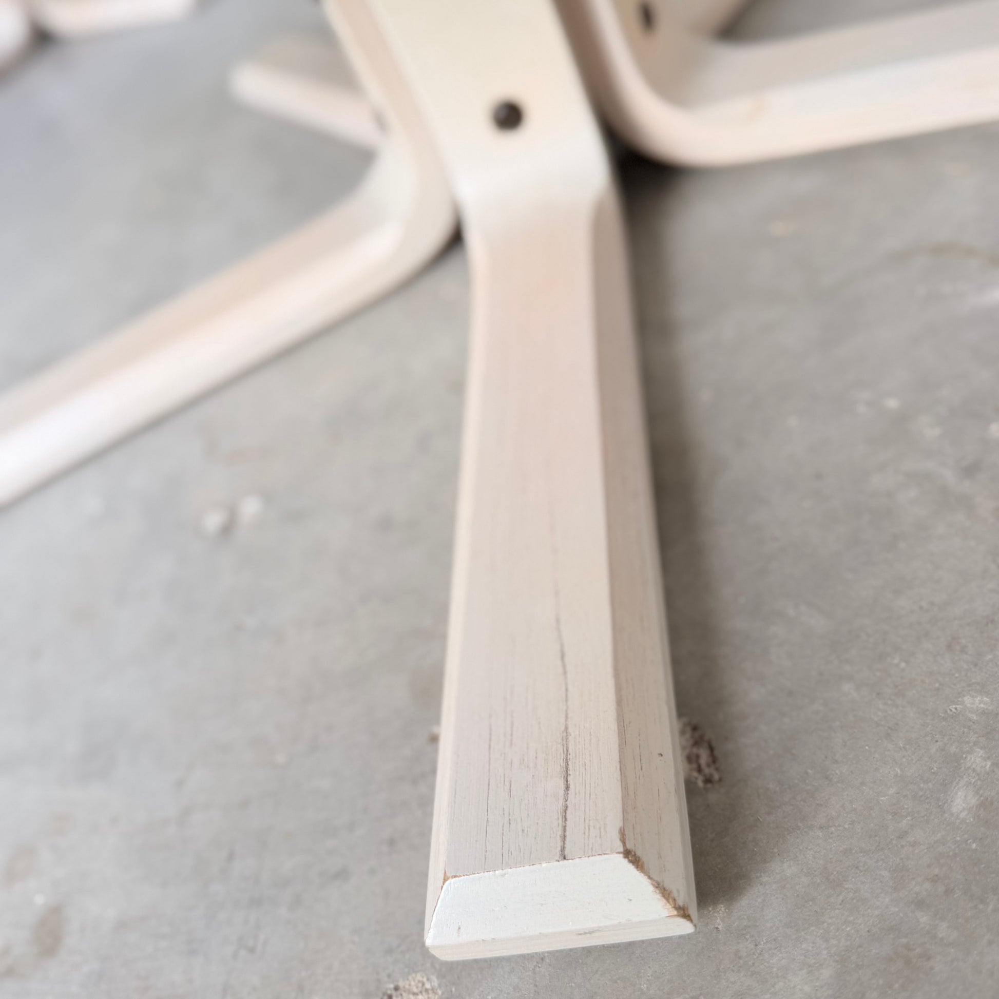 A close-up of a light wooden leg with a beveled edge, from the Pair of Tessa Ferrara Swivel Armchairs (Revive), evokes mid-century Australian style and rests on a smooth gray concrete floor alongside matching legs.