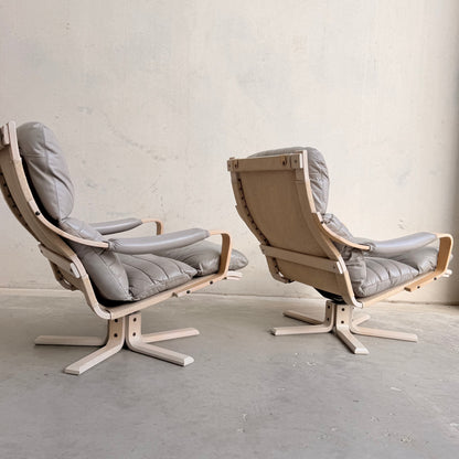 The Tessa Ferrara Lounge Suite – Complete 5-Piece Set (Revive) features light wood frames and gray upholstery; two chairs are set on a concrete floor against a plain wall, one facing forward and the other displaying its back.