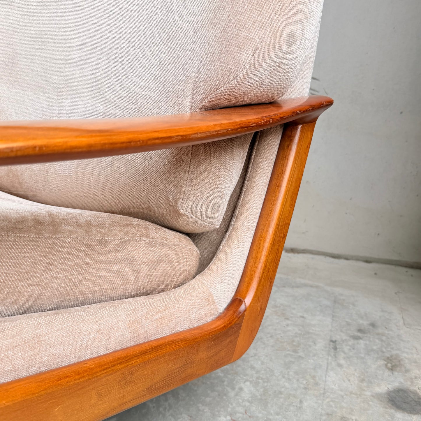 Close-up of a Vintage Mid Century Tessa T21 Swivel Chair (Revive) in cream velvet, featuring a smooth curved wooden frame, set on concrete flooring by a light gray wall—showcasing timeless mid-century design.